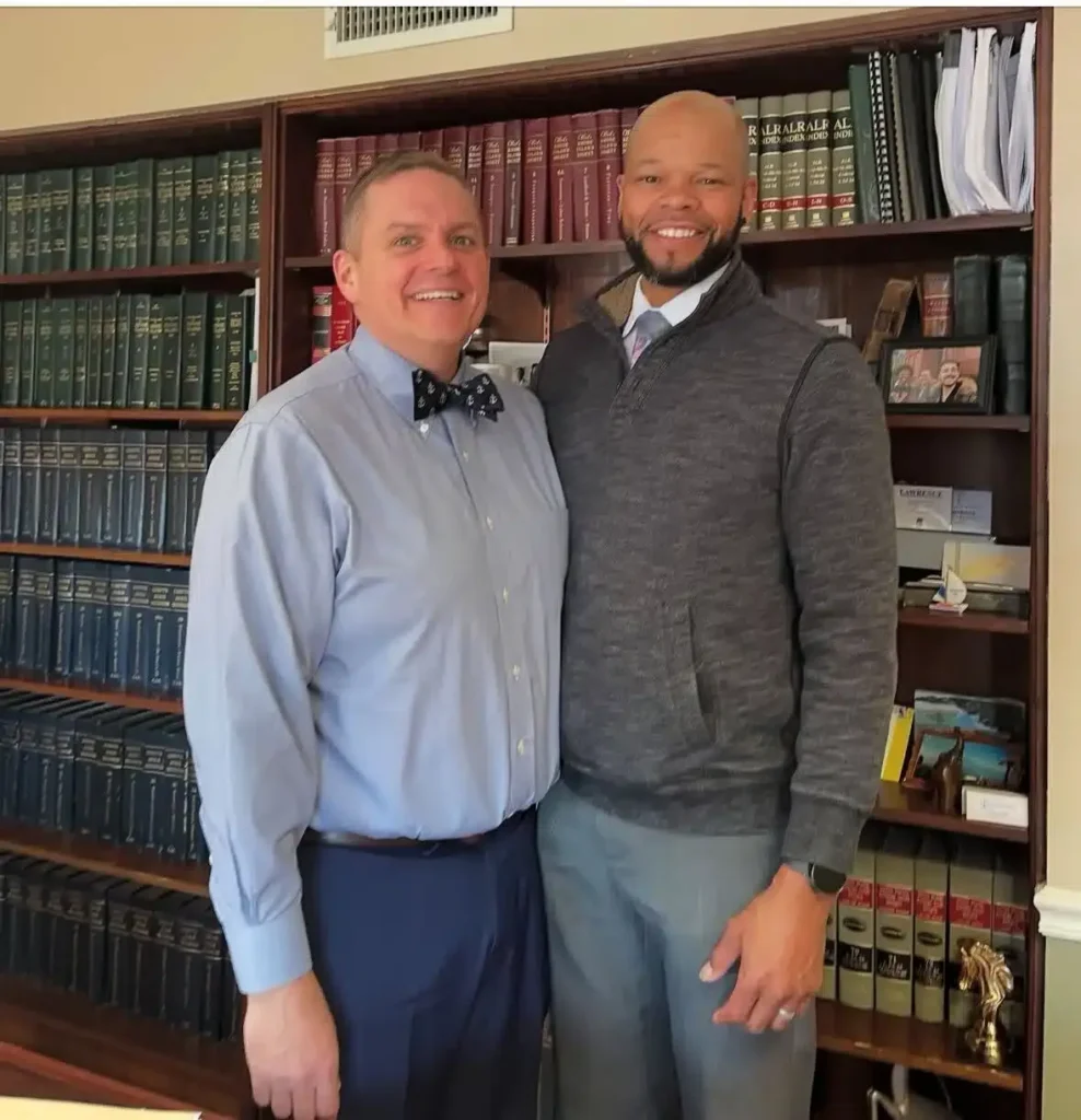 imgi_31_IMG_0218 Two men standing together in an office with bookshelves filled with legal texts in the background.