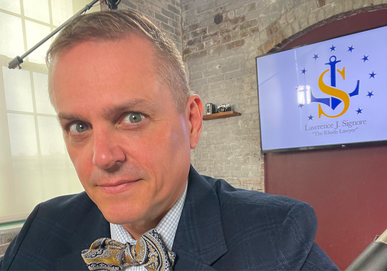 Portrait of attorney Lawrence J. Signore wearing a bow tie in an office setting with a logo in the background. Portrait of attorney Lawrence J. Signore wearing a bow tie in an office setting with a logo in the background.